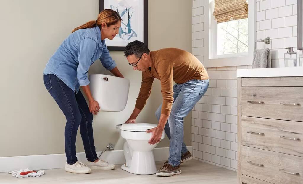 Bathroom remodelers in Dallas installing a new toilet in a tiled white bathroom
